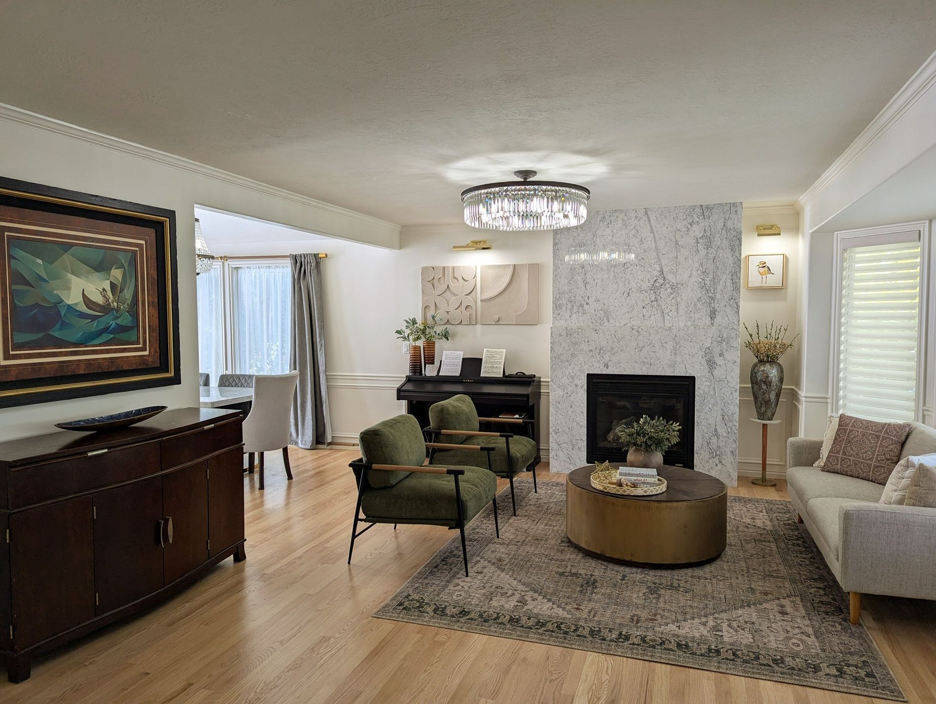 Bright living room with fireplace, green chairs, wood cabinet, and beige sofa on a patterned rug.