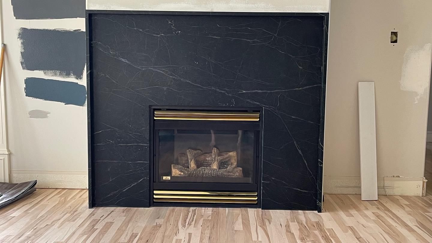 Living room fireplace with black marble surround and brass-trimmed insert, surrounded by paint samples and wood floor