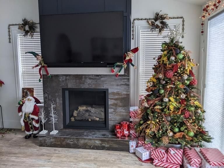 Decorated living room with a TV above a fireplace, Christmas tree, stockings, and holiday décor