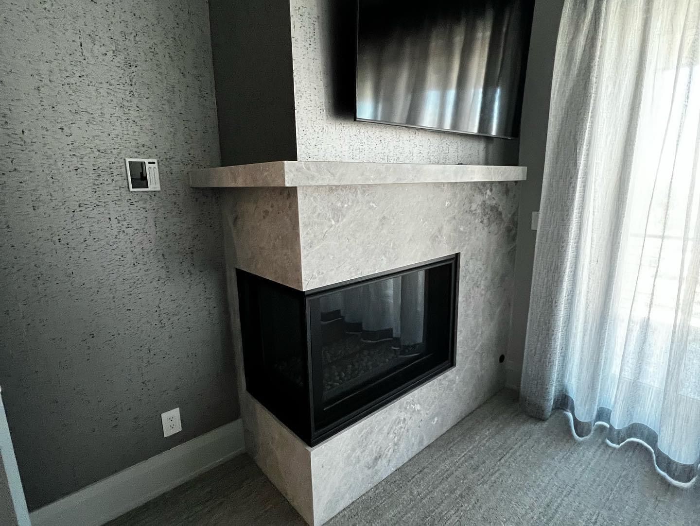 Corner fireplace with light stone surround, black glass insert, and sheer curtains beside it