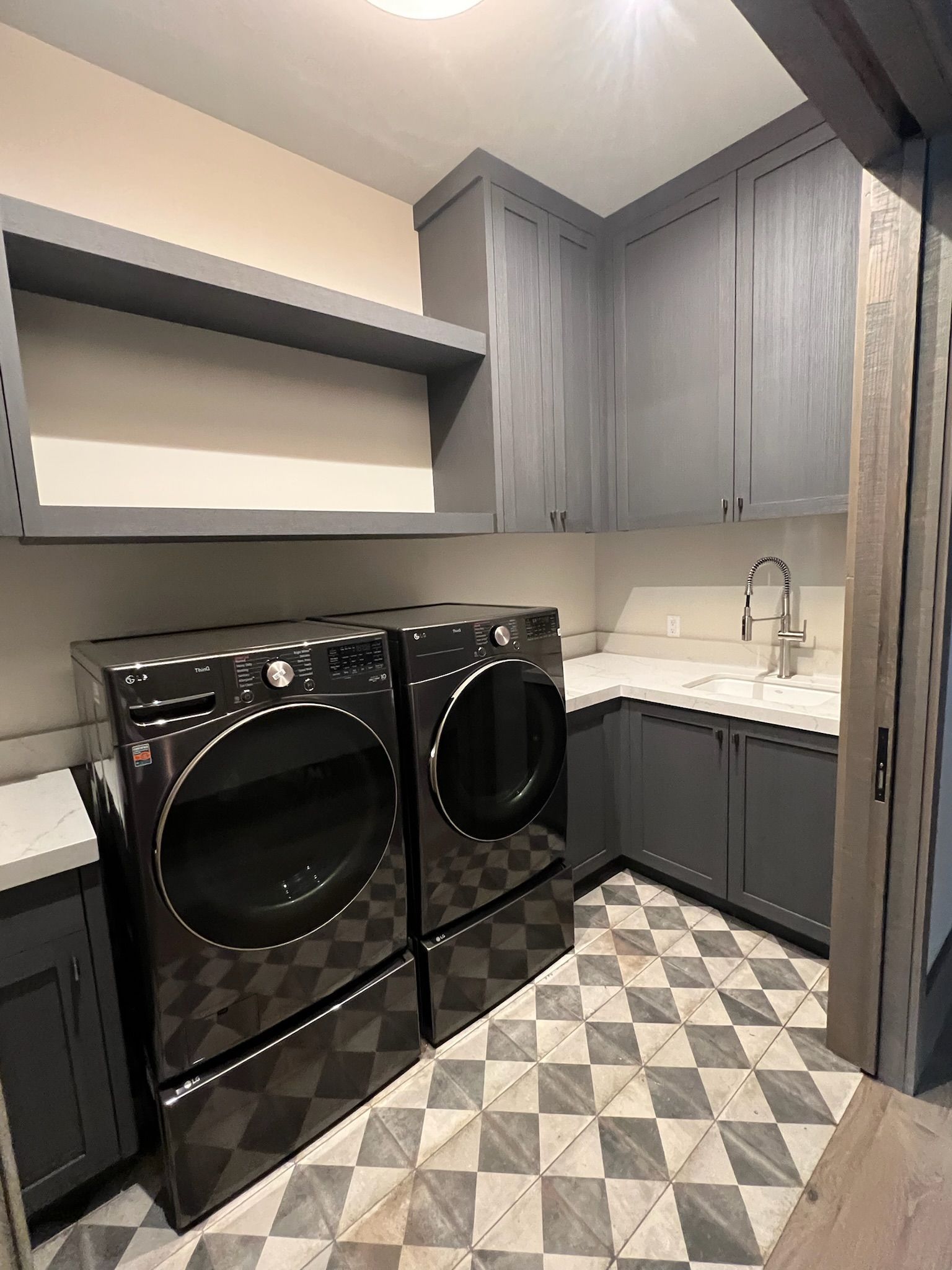 Modern laundry room with gray cabinets, black washer and dryer, white countertop, and patterned tile floor