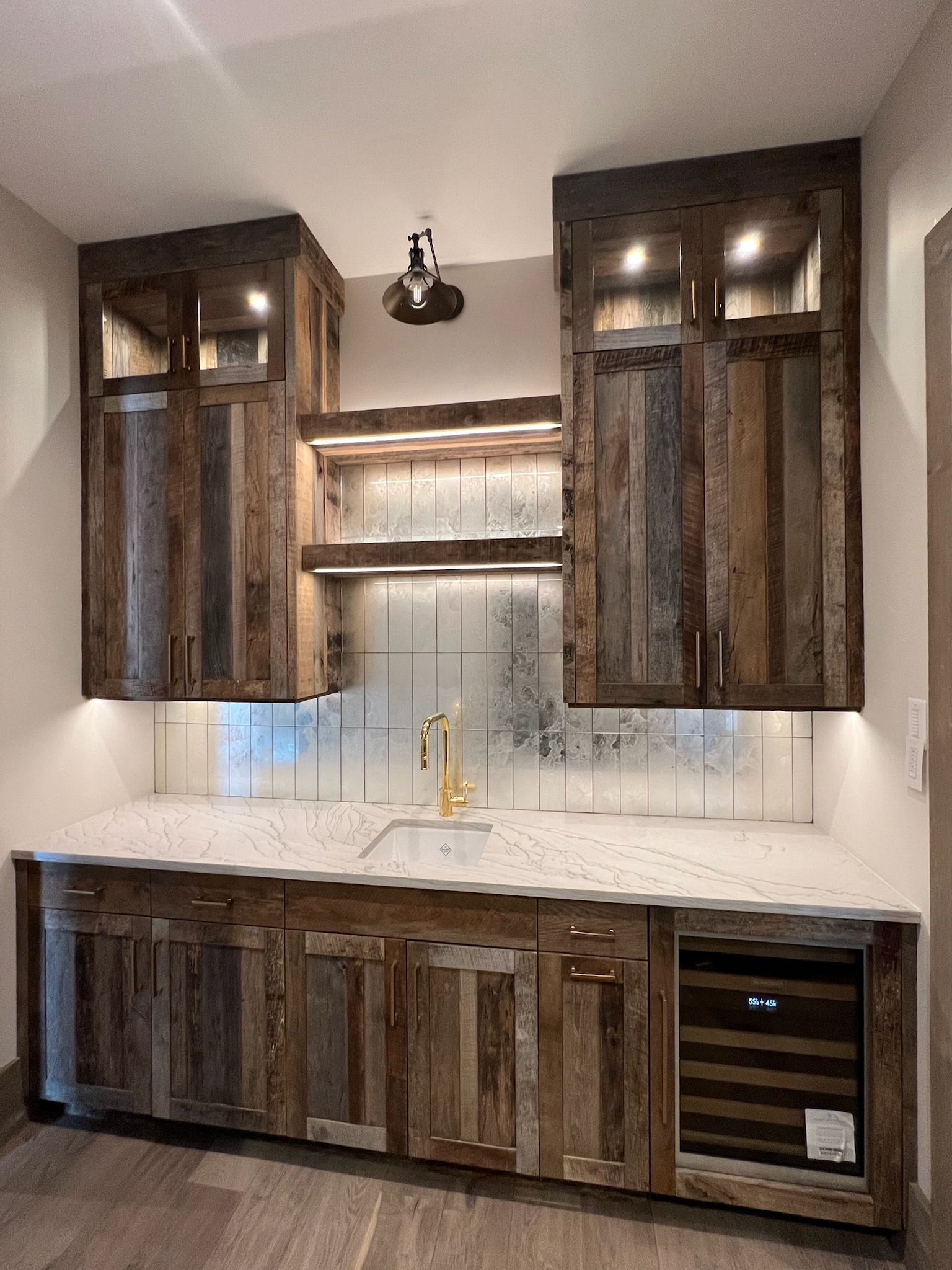 Wooden kitchen cabinets with white backsplash, countertop, and built-in wine cooler under warm lights