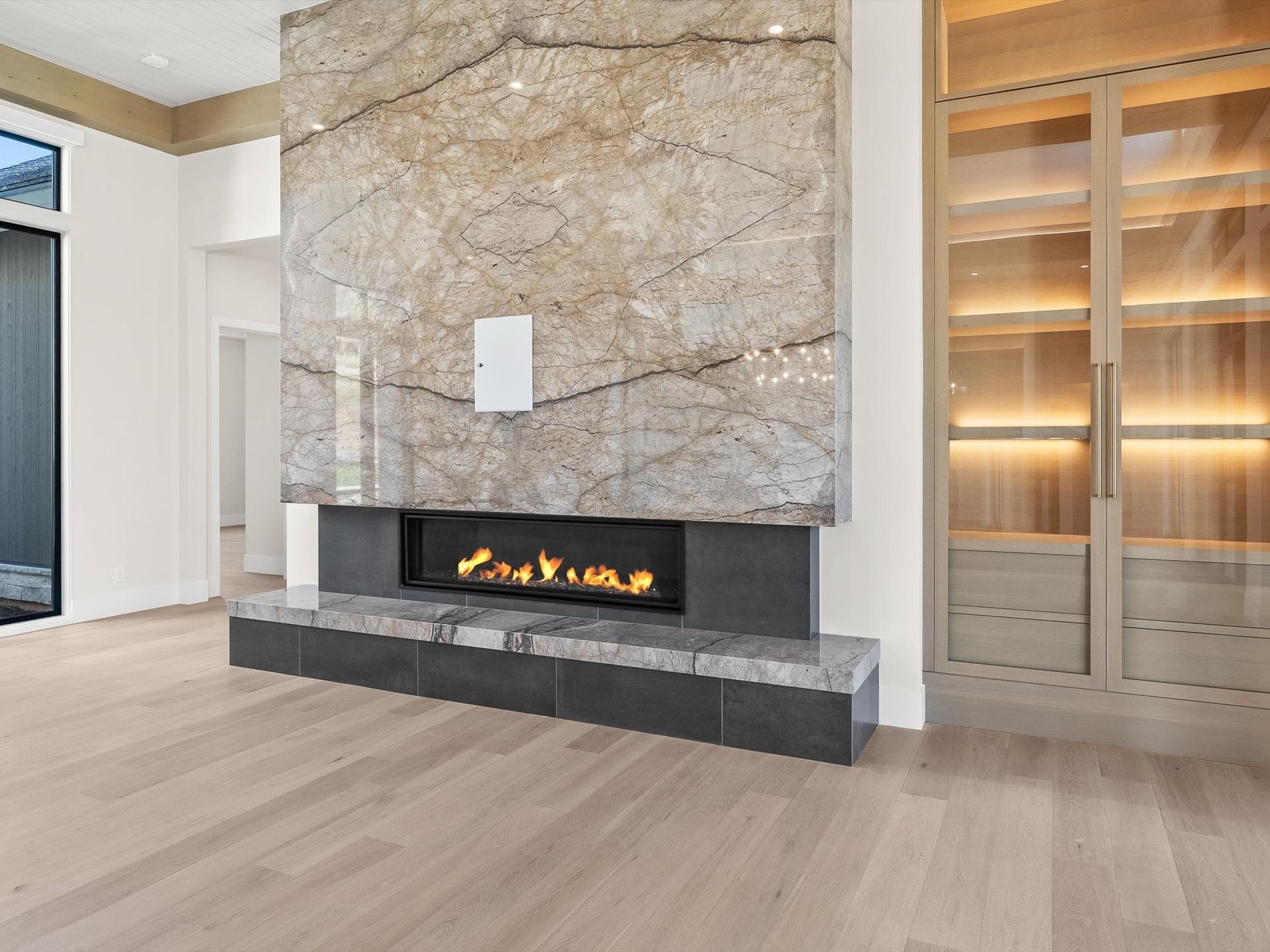 Modern living room with a stone fireplace, built-in shelves, and light wood floors
