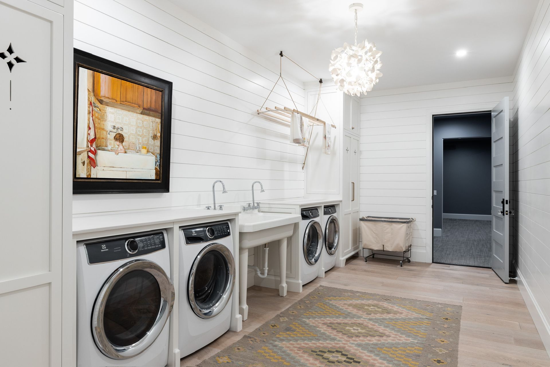 Bright laundry room with front-loading washer and dryer, utility sink, wall hooks, bench, and patterned rug.