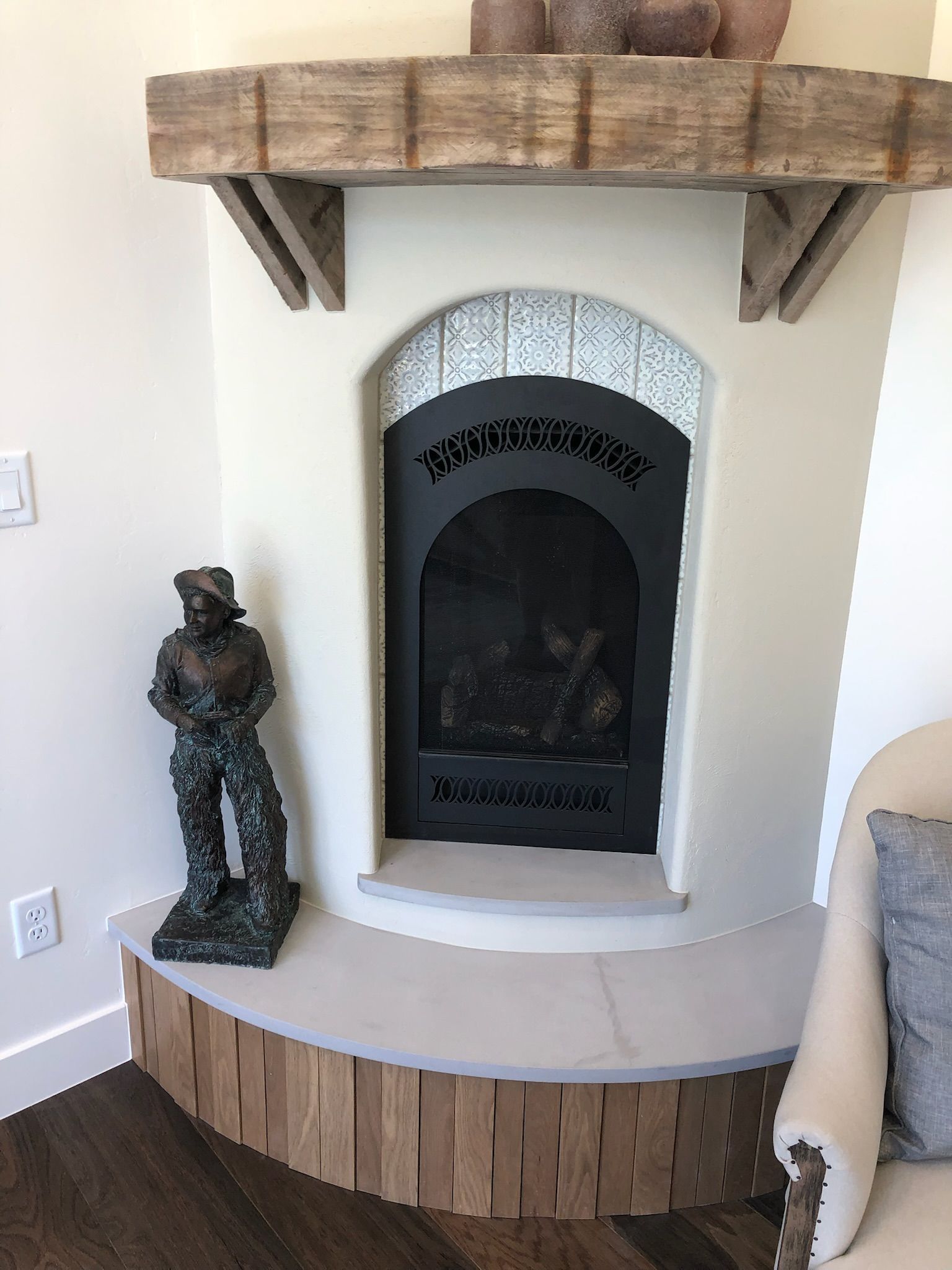 Corner fireplace with white surround, rustic wood mantel, stone hearth, and a bronze figurine beside it