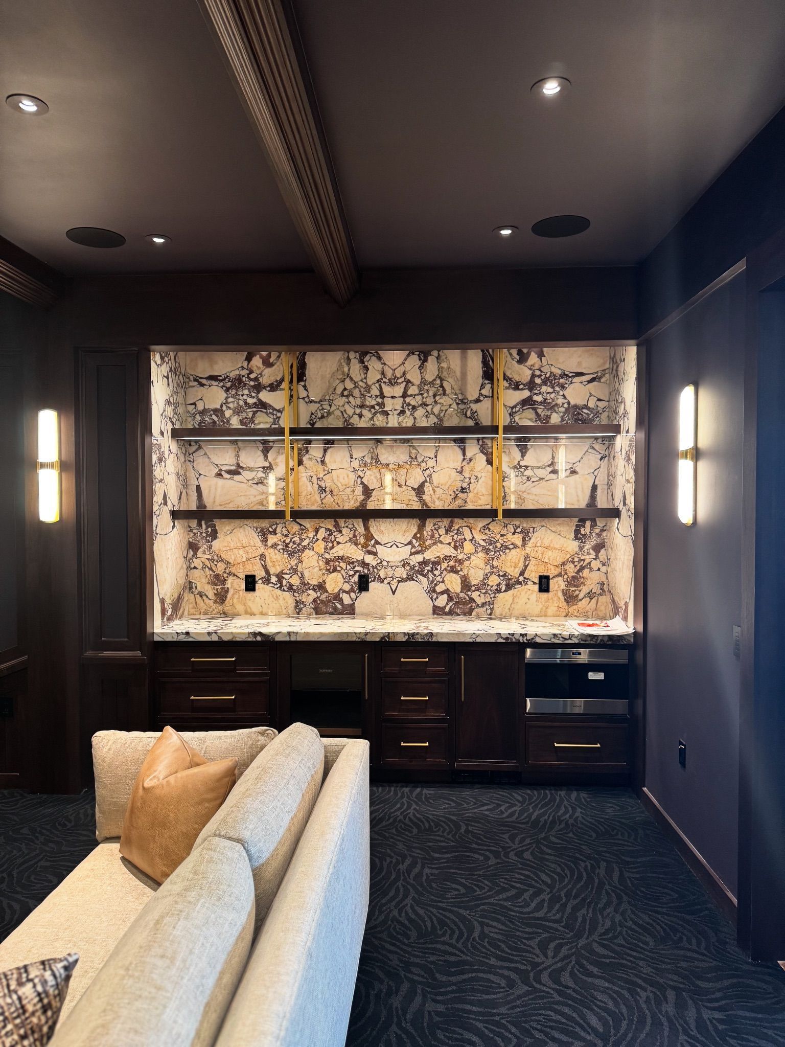 Modern lounge with dark walls, patterned wall art, built-in cabinets, and a cream sofa in the foreground
