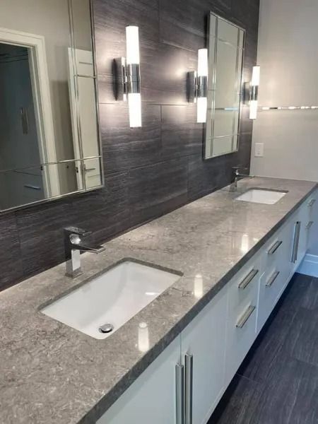Bathroom with gray countertop, white cabinets, and vertical wall-mounted lights above rectangular mirrors.