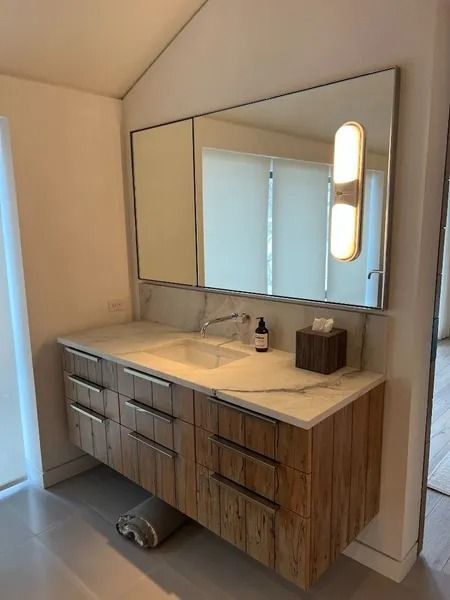 Bathroom with wood vanity, marble countertop, large mirror, and wall-mounted light fixture.