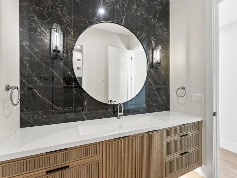 Bathroom with black marble tile, a round mirror, and a wood vanity with a white countertop.