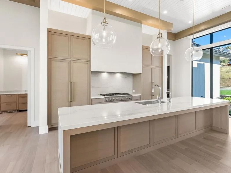 Modern kitchen with beige cabinets, marble countertops, large island, and globe pendant lights.