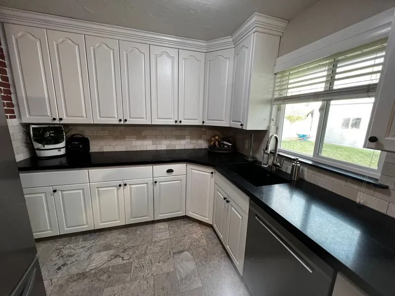 White kitchen cabinets with black countertops and stainless steel appliances.