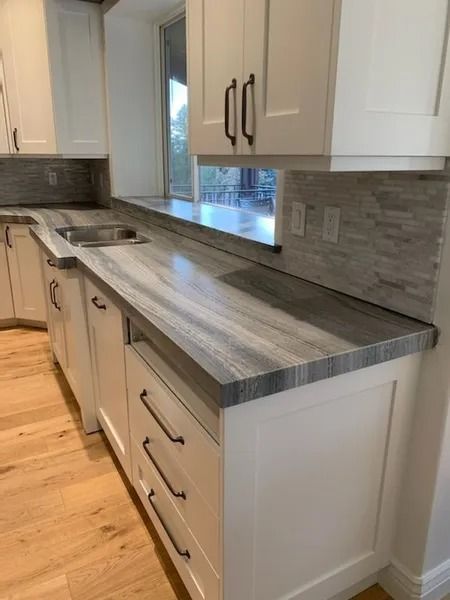 White kitchen cabinets with gray countertops and backsplash; light wood floor.