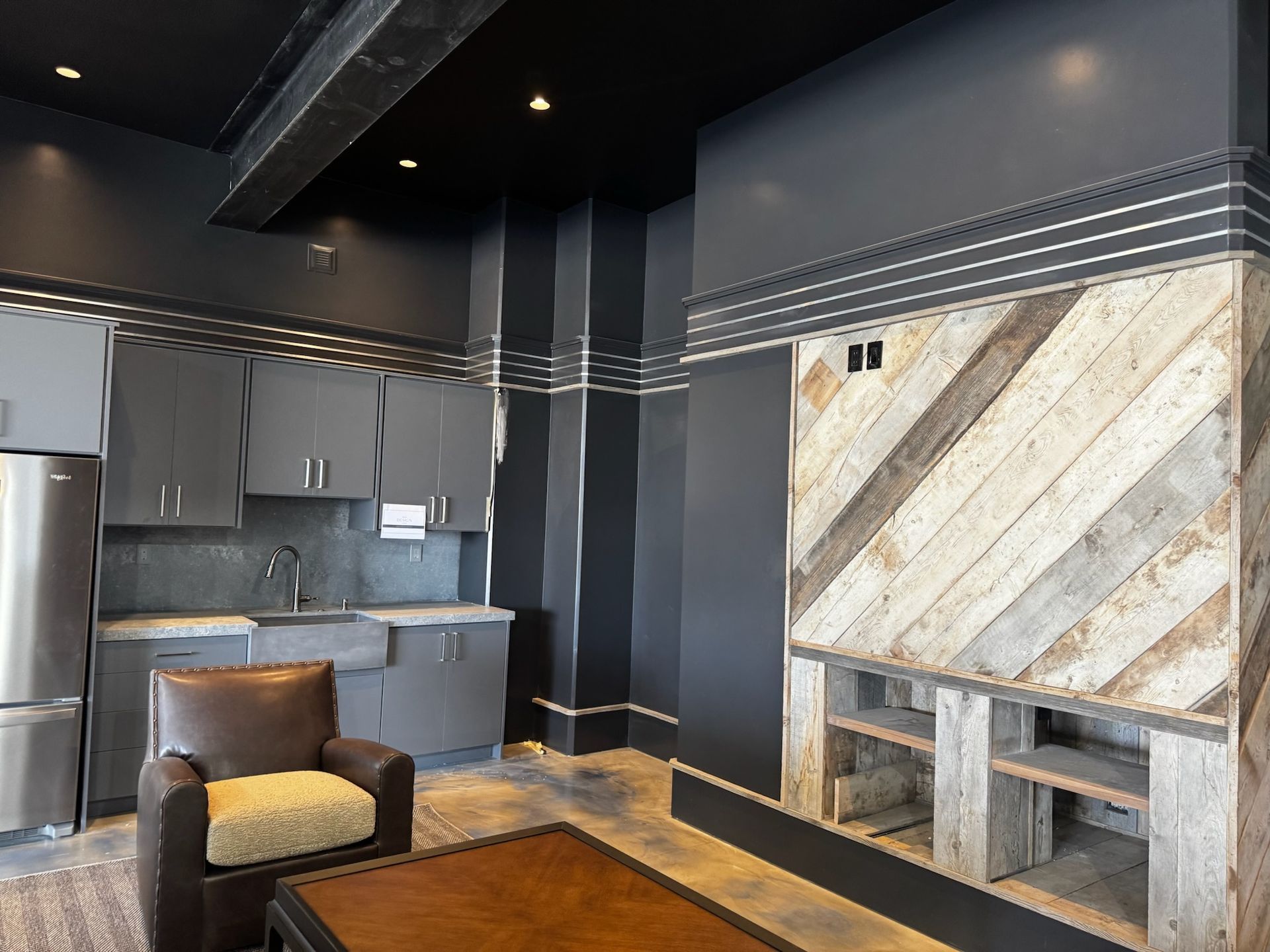 Modern living room with black walls, gray cabinets, a stone fireplace, and a leather chair on a patterned rug