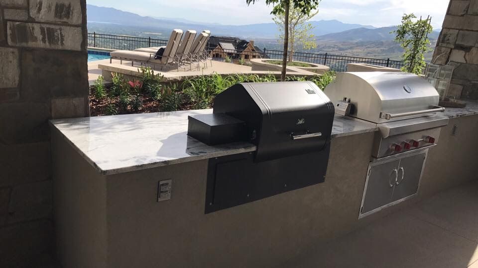 Two outdoor grills on a patio with mountains and a lake in the background