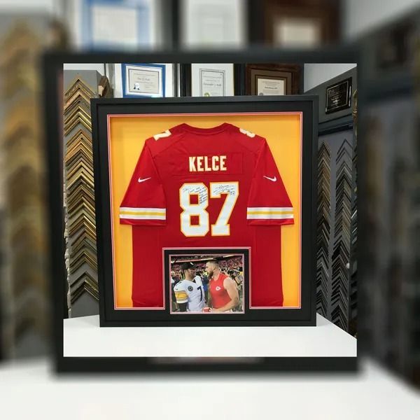 Framed red Kelce #87 jersey display with an inset photo, in a wall-mounted memorabilia case.