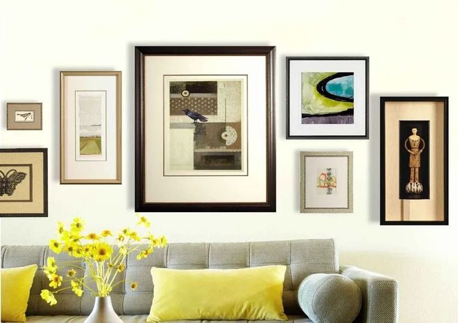 Framed abstract art gallery wall above a light sofa with yellow pillows and flowers
