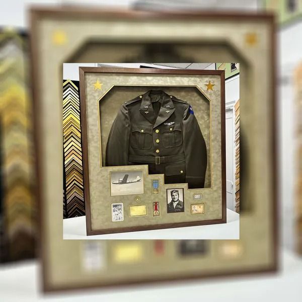 Framed military uniform display with medals, badges, and a portrait on a beige background