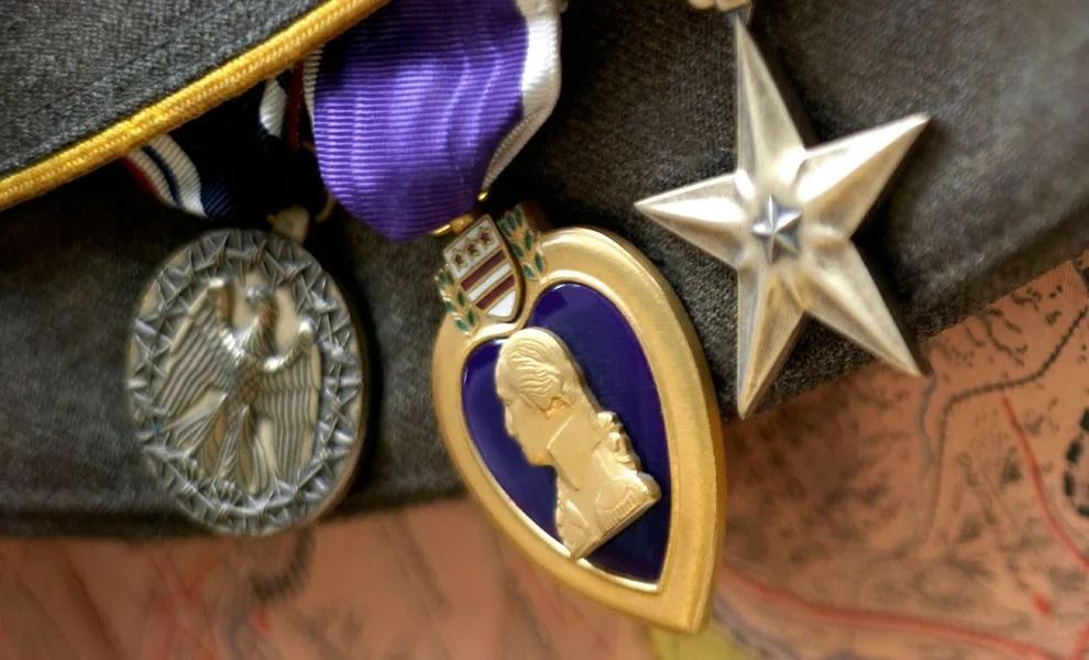 Close-up of military medals and ribbons on a uniform, including a purple and gold medal and a silver star.