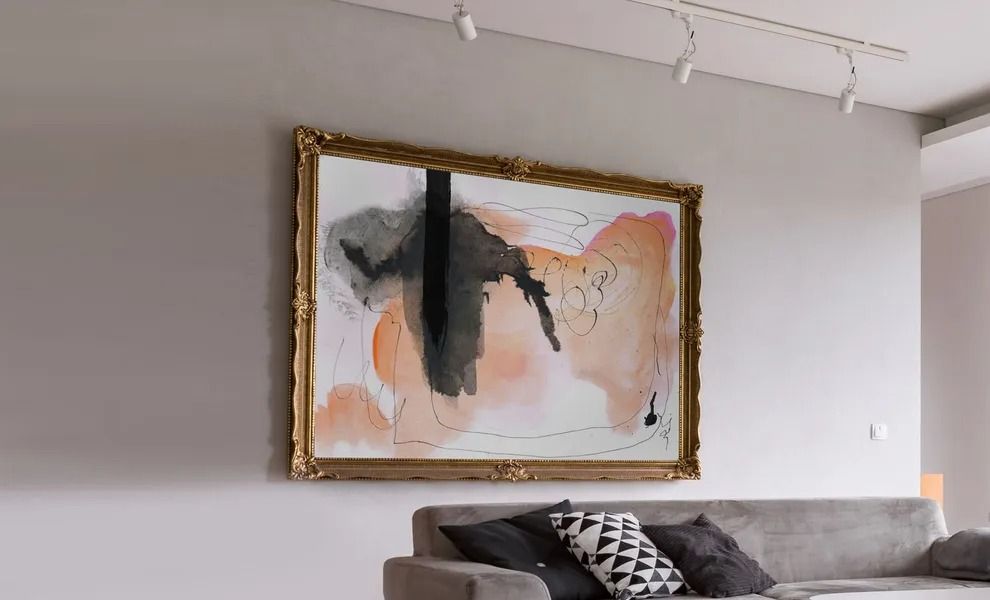 Modern living room with a large abstract painting in gold frame above a gray sofa.