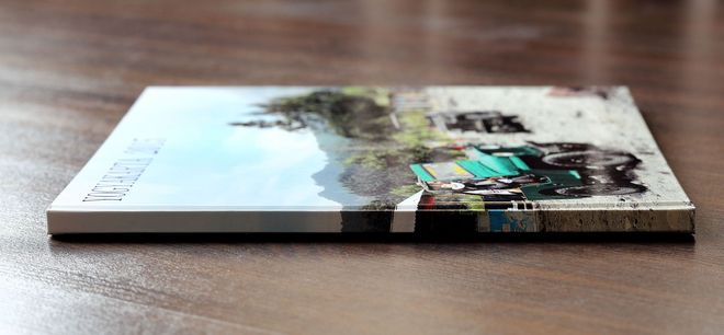 A glossy printed photo book lying on a wooden table, with a white cover and a colorful image on the spine.