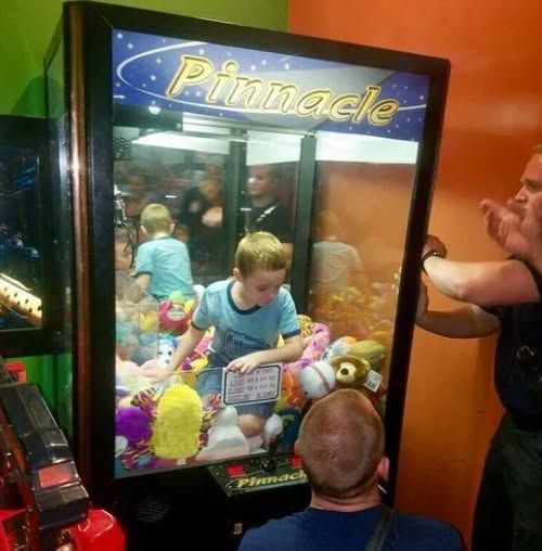 People playing a claw machine arcade game with stuffed prizes visible inside.
