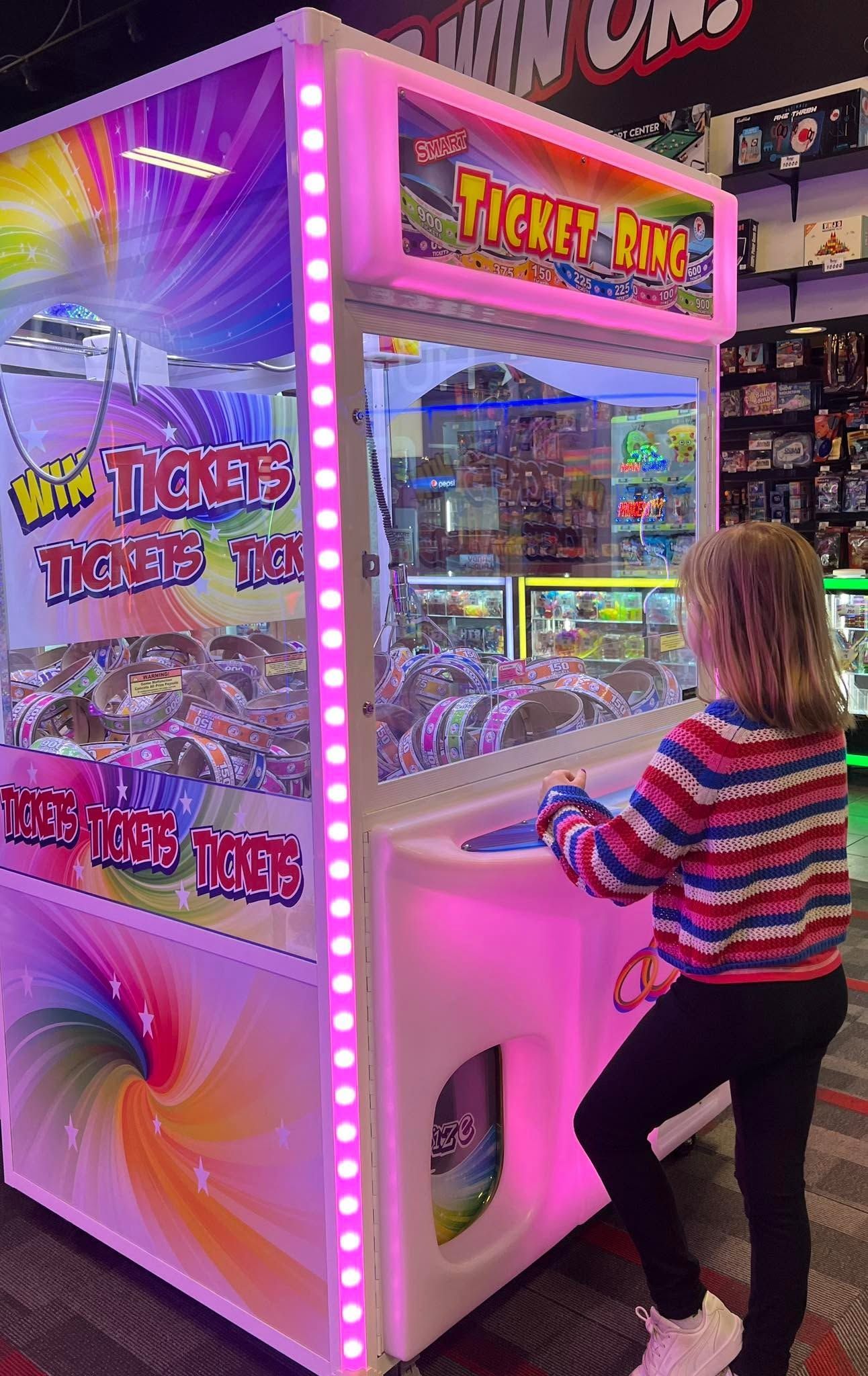 Child playing a bright pink ticket arcade game with flashing lights in an arcade