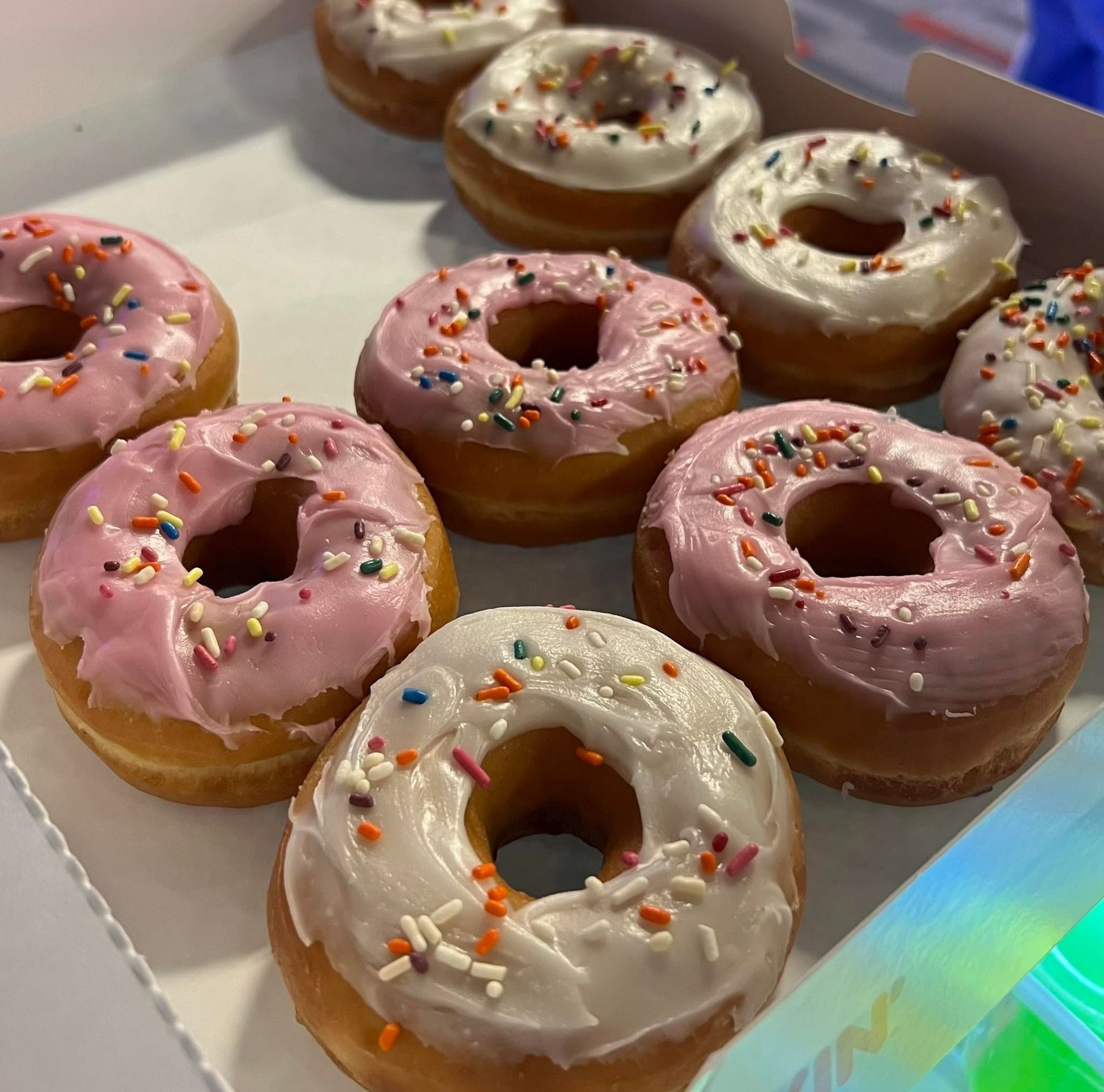 Tray of iced donuts with pink, white, and tan frosting topped with colorful sprinkles