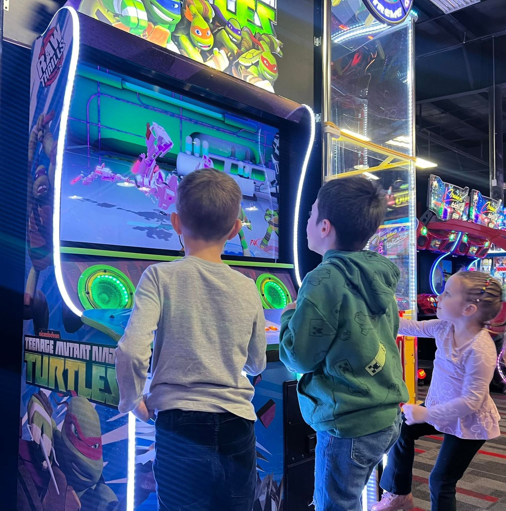 Three children playing a colorful arcade game with bright neon lights