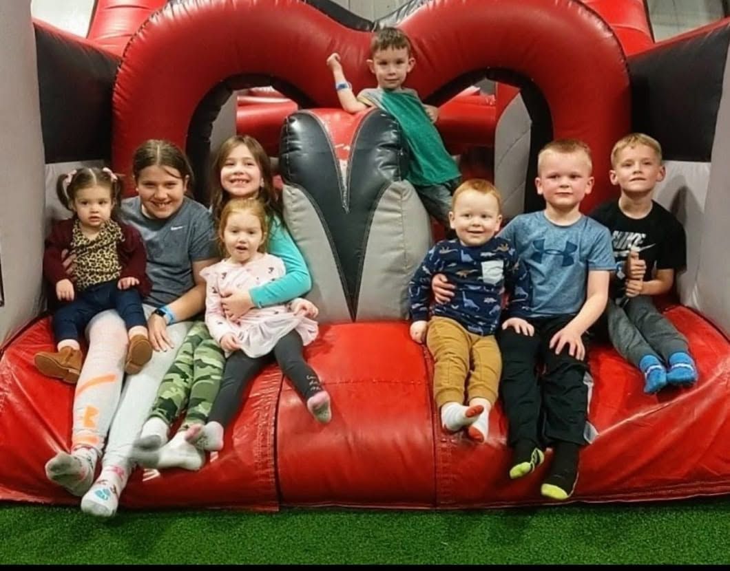 Children sitting on a red inflatable play structure, smiling indoors