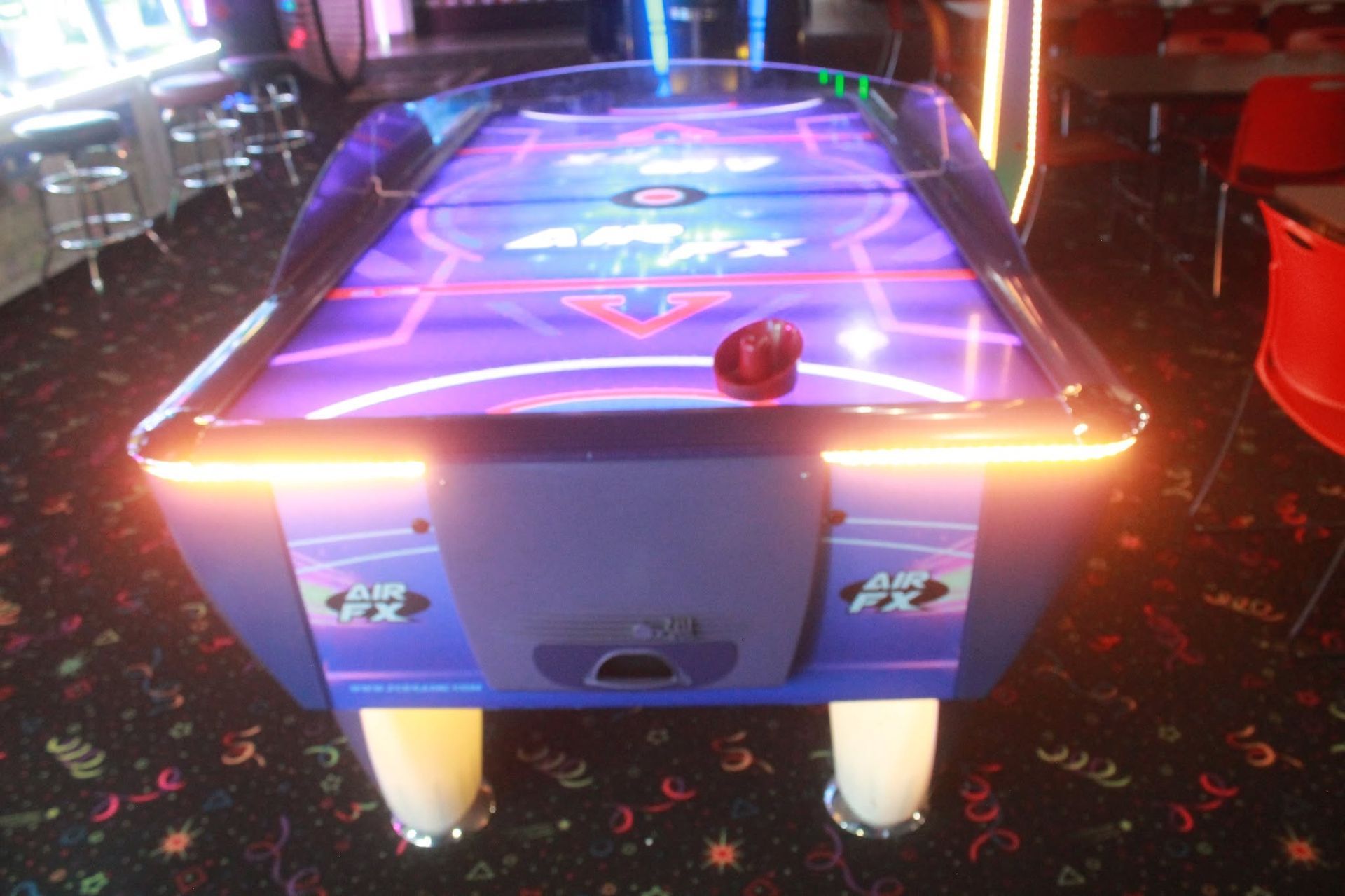 Glowing air hockey table in a neon-lit arcade, with a puck near the front edge.