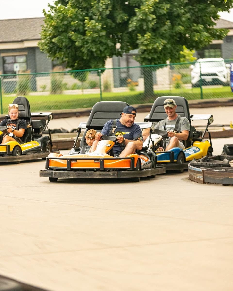 People riding bumper cars at an outdoor amusement ride, with two cars side by side on a track