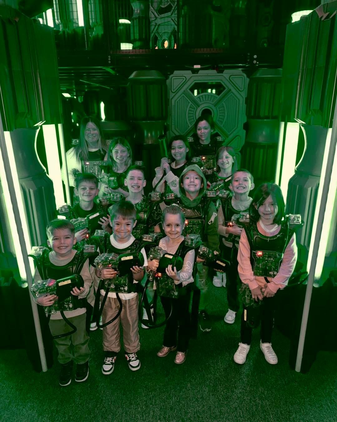 Group of children posing in a green-lit futuristic corridor, wearing matching black outfits