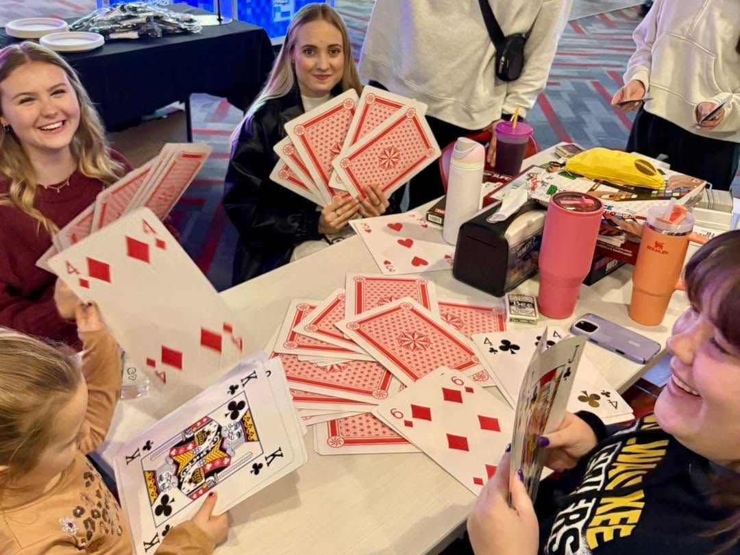 People around a table playing cards, with a large fan of playing cards in the foreground.