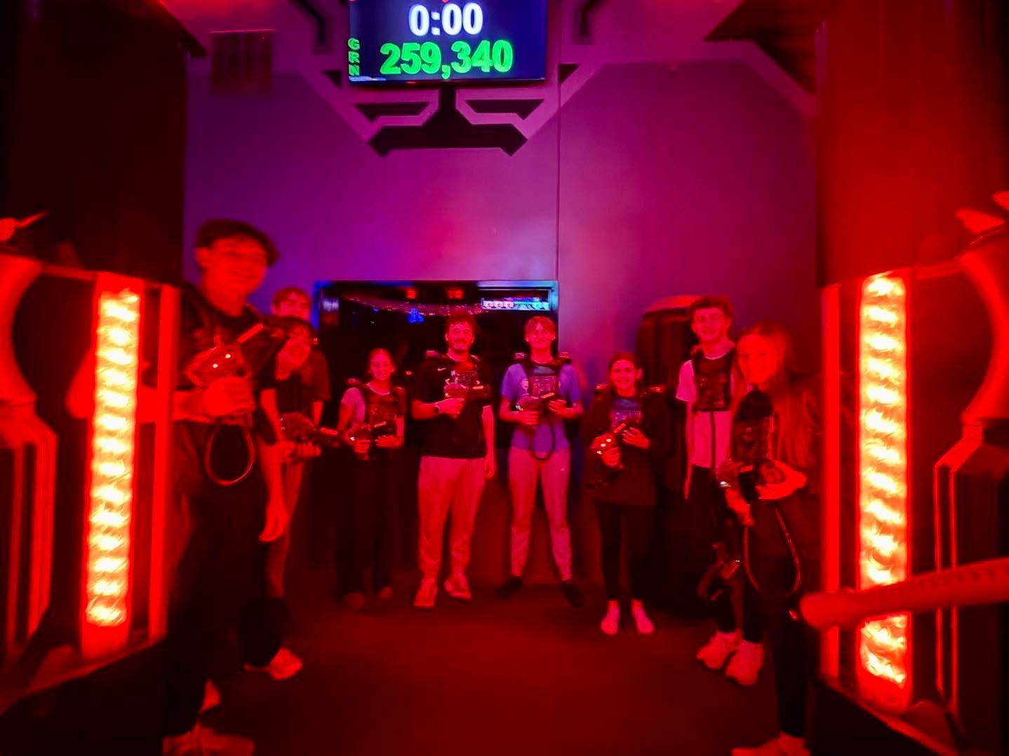 People standing in a red-lit arcade game room with a digital timer overhead