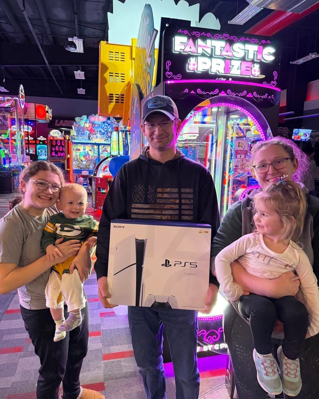 Family posing with prizes at an arcade, standing before a neon-lit prize wall.