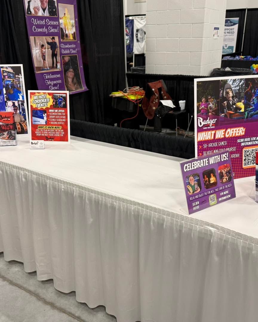 Convention booth with a white tablecloth, colorful posters, and flyers displayed on black drapes.