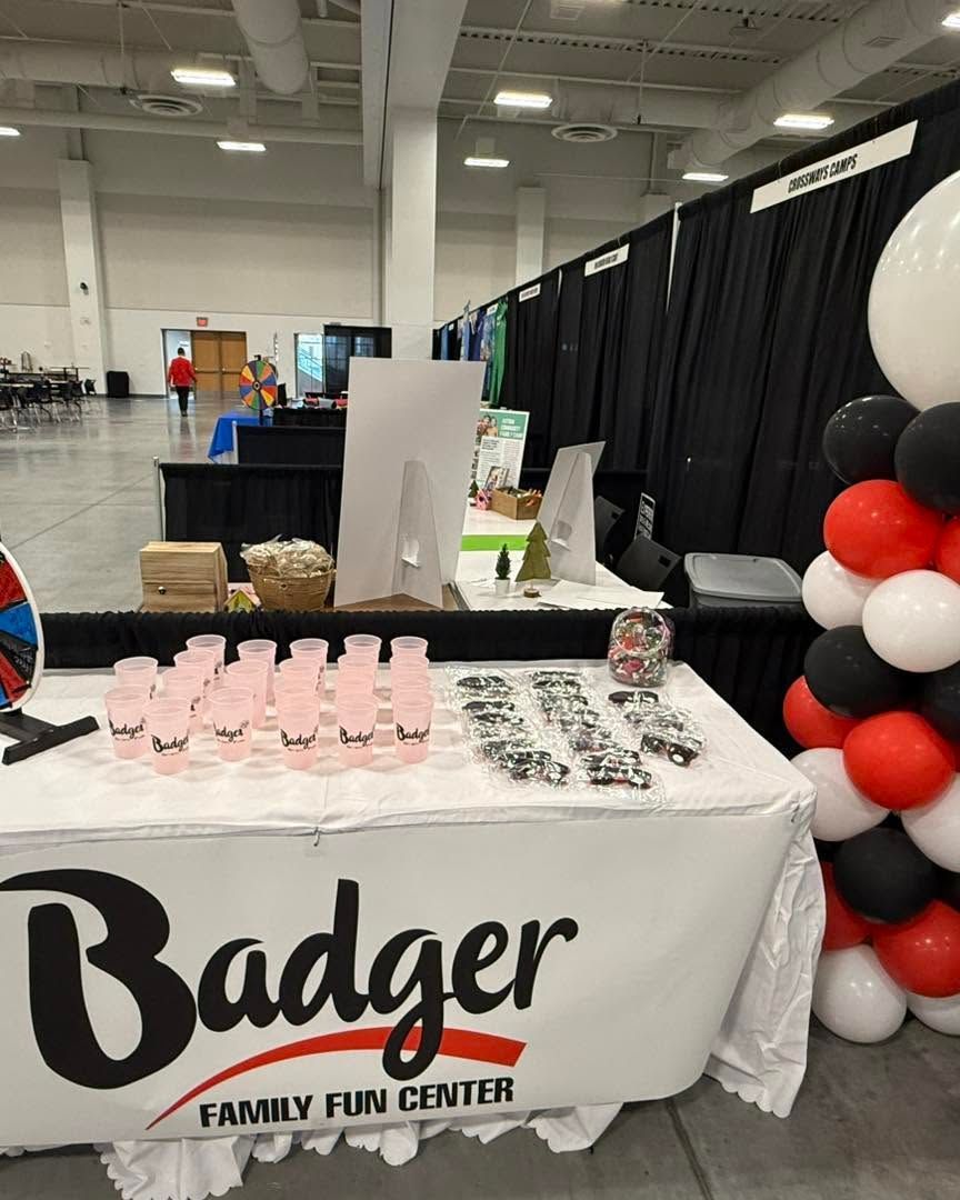 Badger Family Fun Center booth with pink treats, black curtains, and red-black balloon column