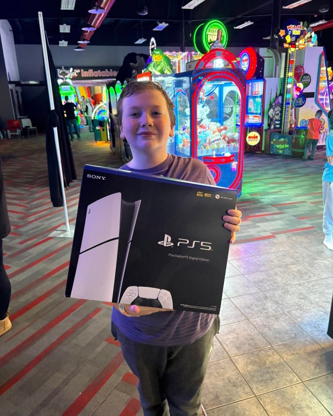 Person holding a PS5 box in an arcade with colorful game machines in the background