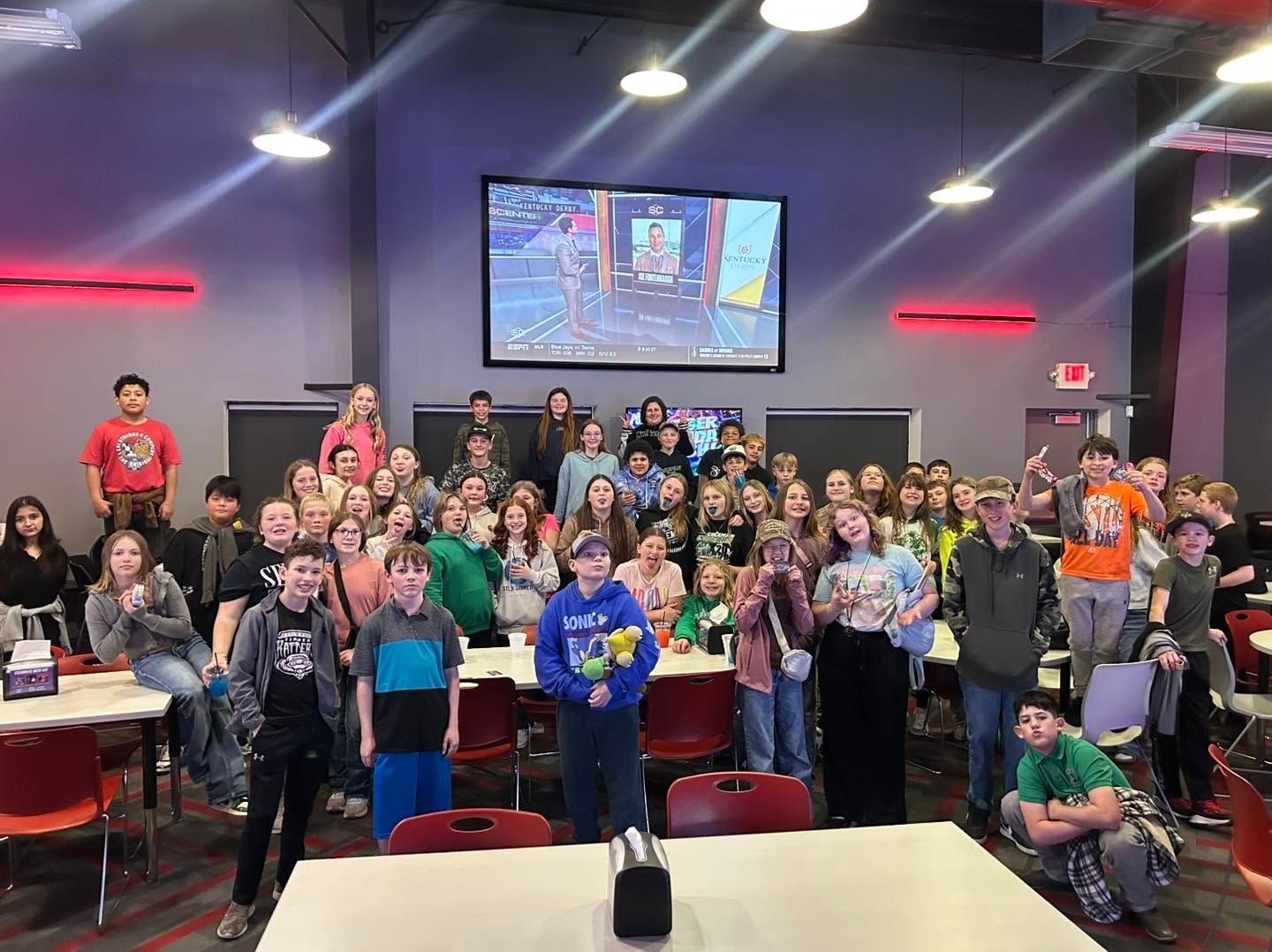 Group of people posing in a recreation hall with arcade screens and neon lights, smiling for a group photo.