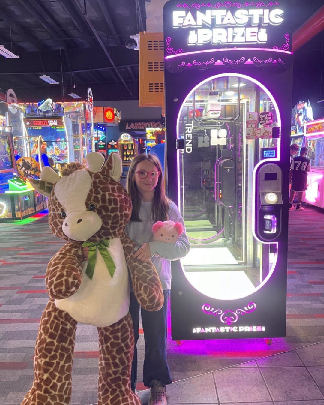 Woman standing beside giant stuffed giraffe in neon-lit arcade prize game area