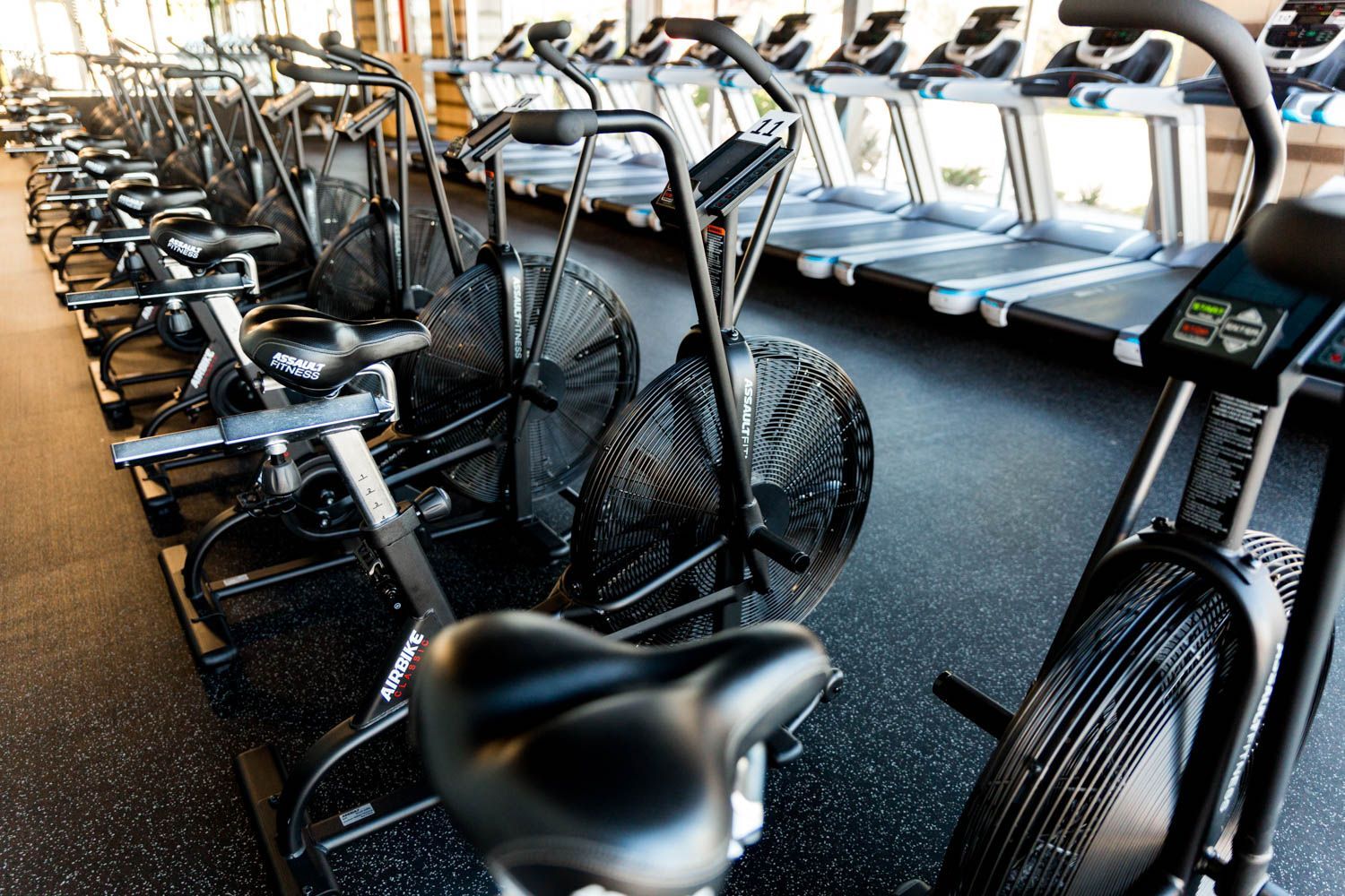 Rows of stationary bikes and treadmills in a brightly lit gym.