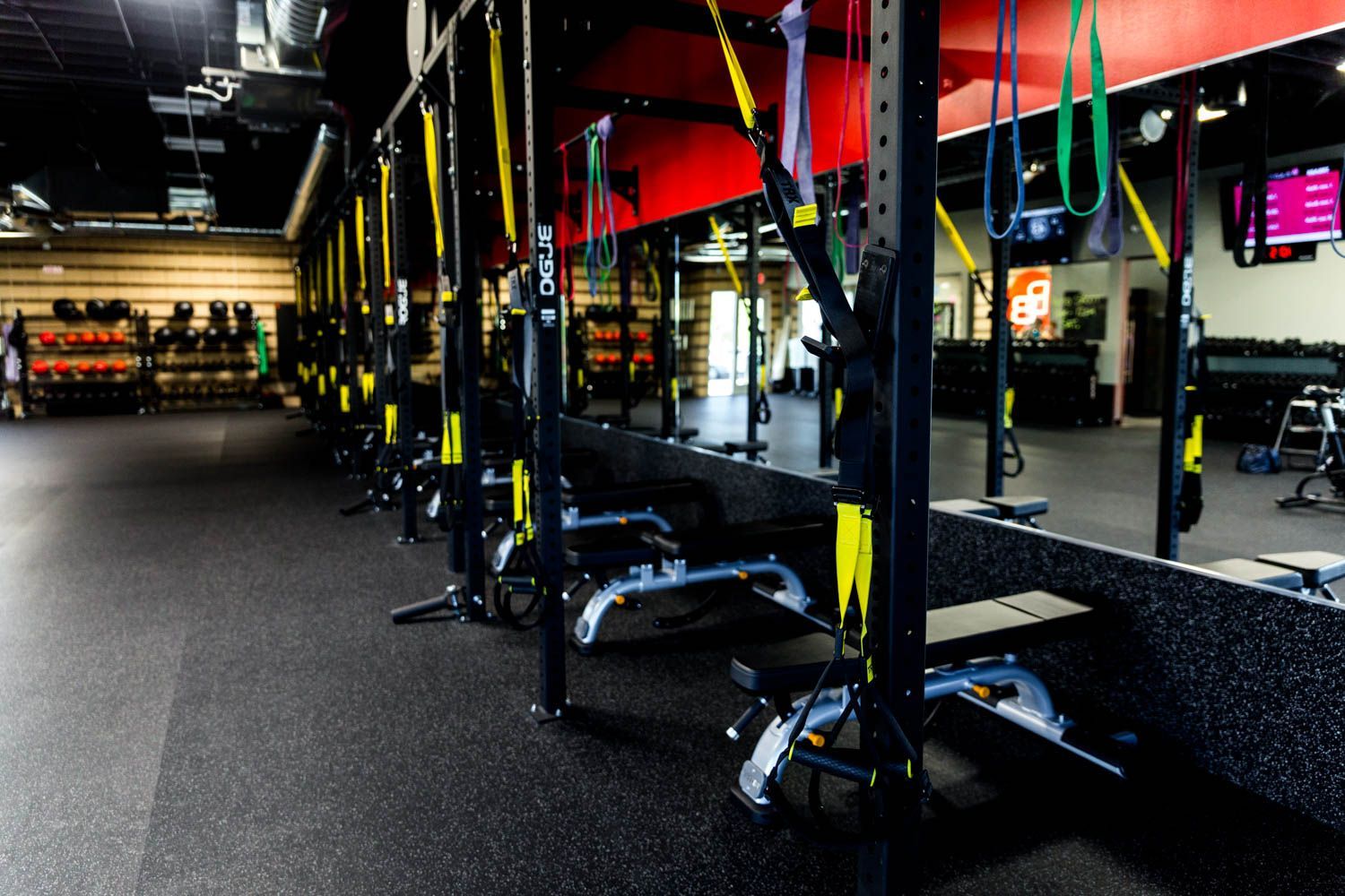Gym interior with black equipment racks, rows of row machines, and suspension trainers.