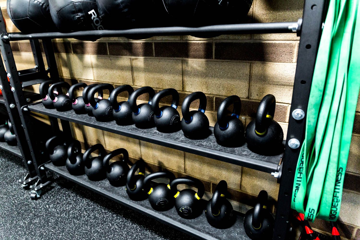 Black kettlebells arranged on shelves in a gym.
