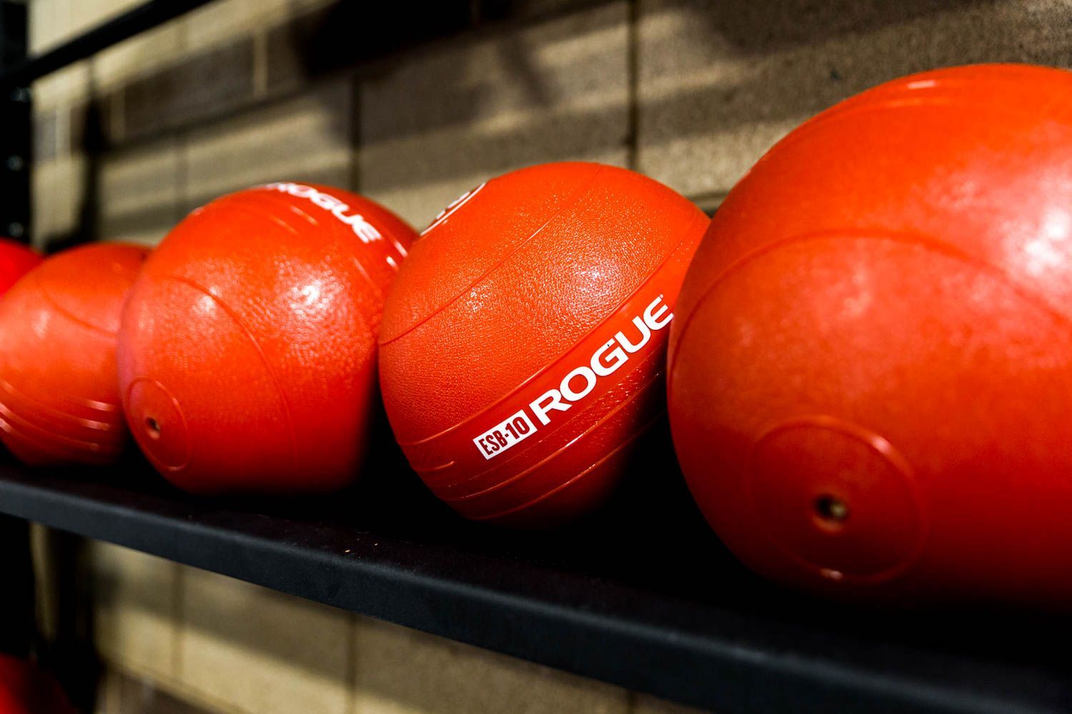 Red Rogue medicine balls on a black shelf in a gym.