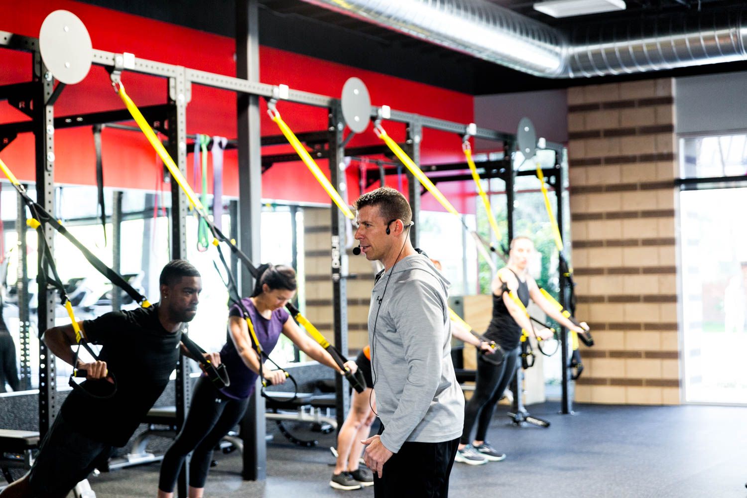 People exercising with suspension straps in a gym, led by an instructor.