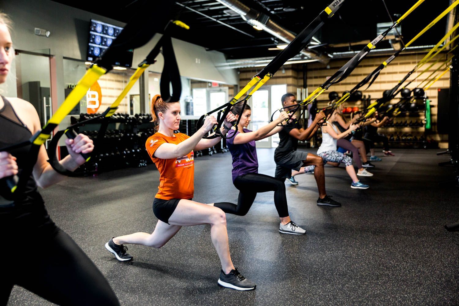 People doing lunges with TRX suspension trainers in a gym.