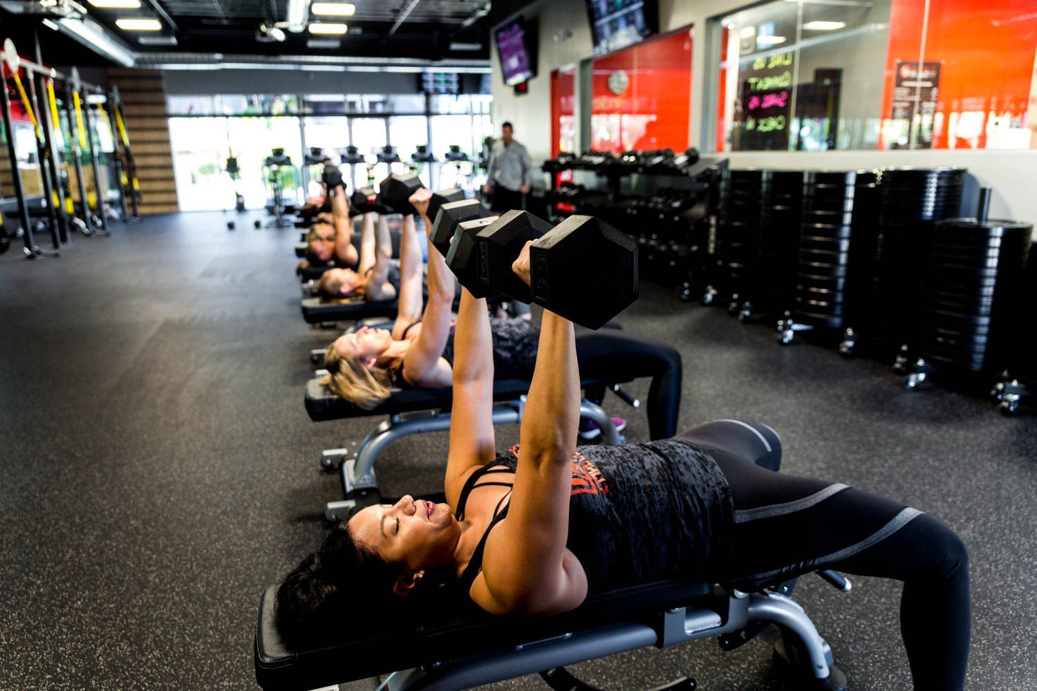 People lifting dumbbells while lying on benches in a gym.