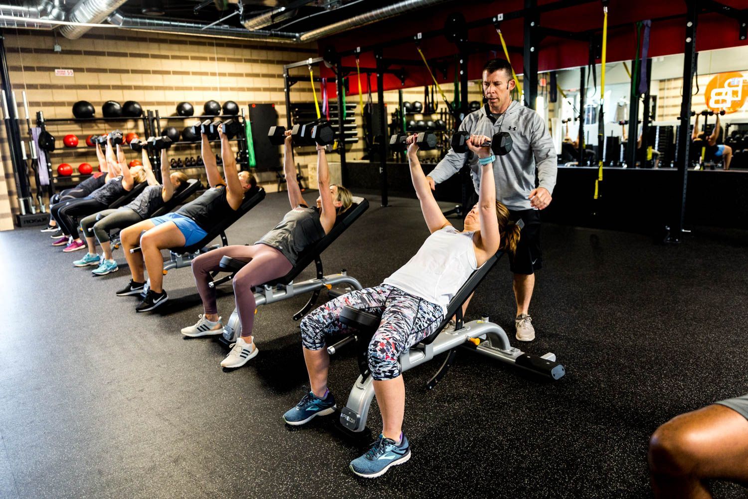 People in gym lifting weights with instructor.