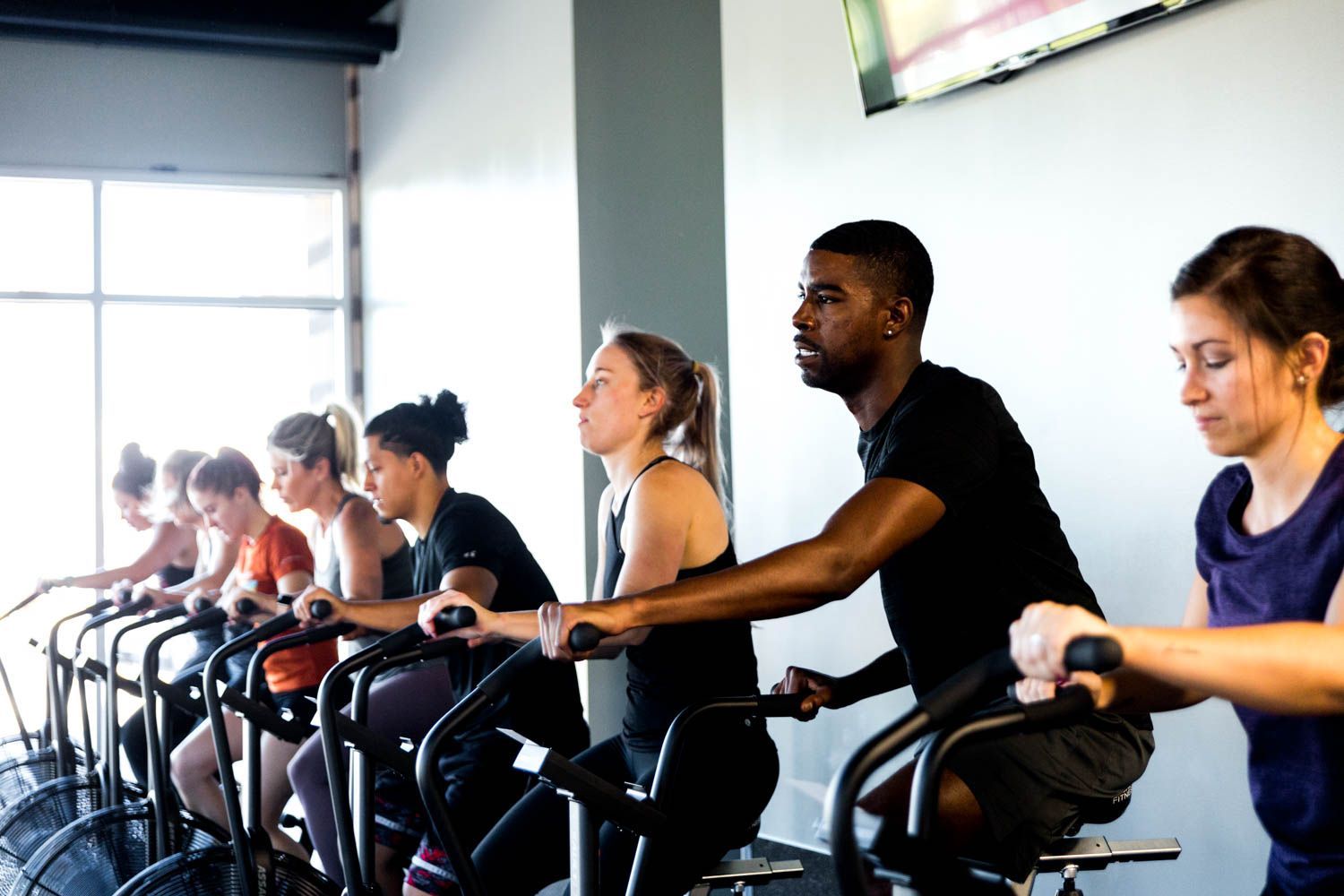 People cycling on stationary bikes in a gym, exercising indoors.