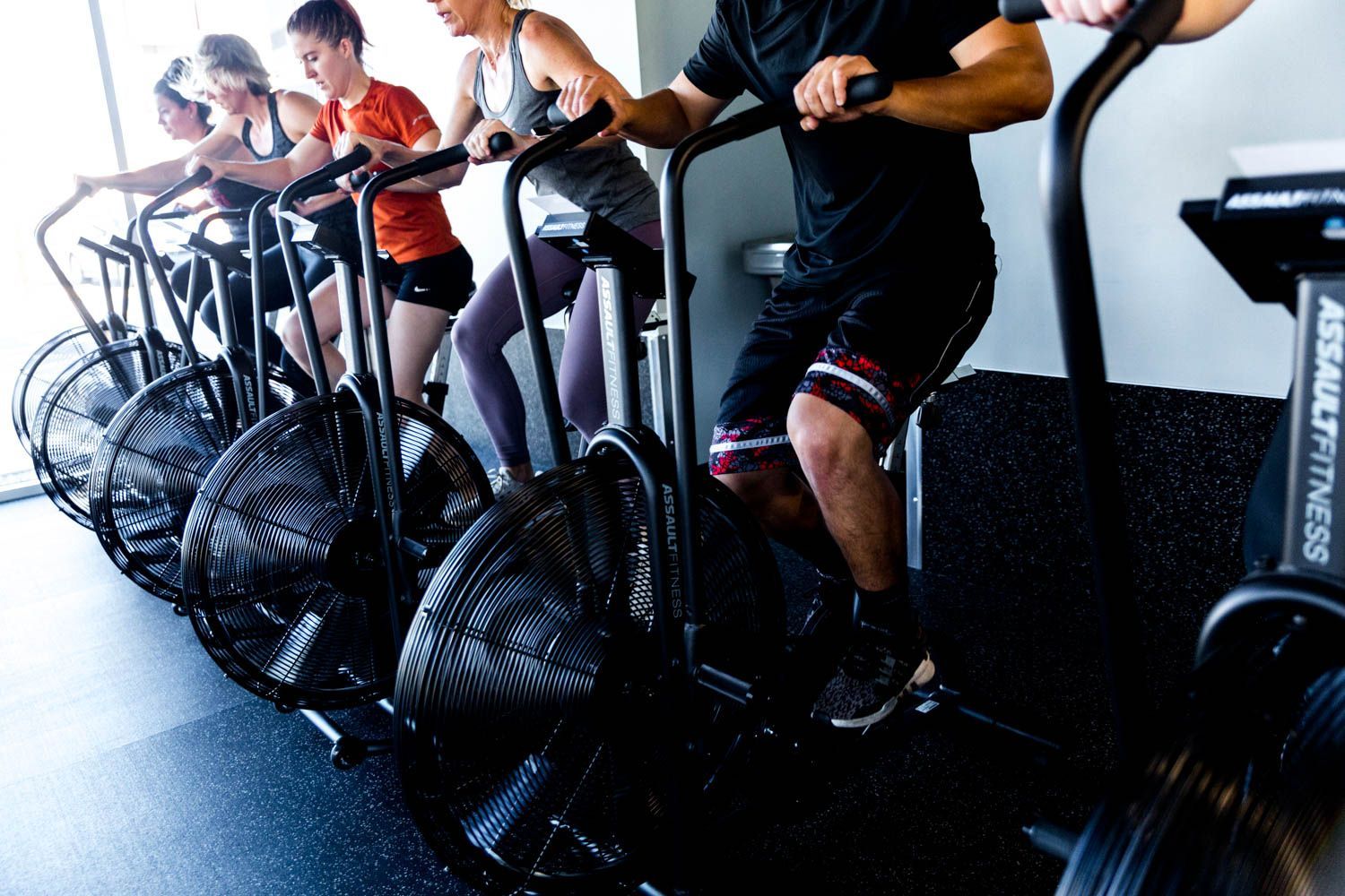 People working out on fan bikes in a gym.